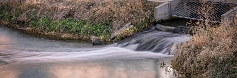 Agua que sale de una rejilla de hormigón hacia un río.