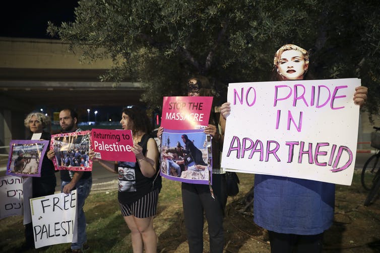 Un manifestante en primer plano sostiene un letrero que dice `` sin orgullo por el apartheid '', mientras que otros llevan carteles como Palestina libre durante una protesta frente al Festival de la Canción de Eurovisión 2019 en Tel Aviv, Israel.