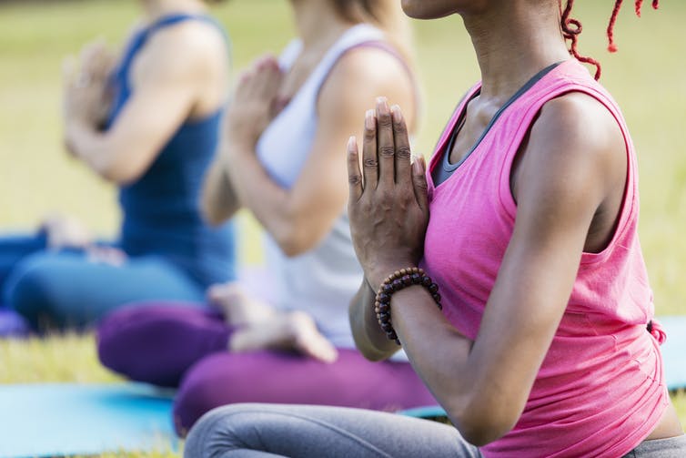 Tres diversas mujeres practicando yoga al aire libre, con una mujer negra en el foco