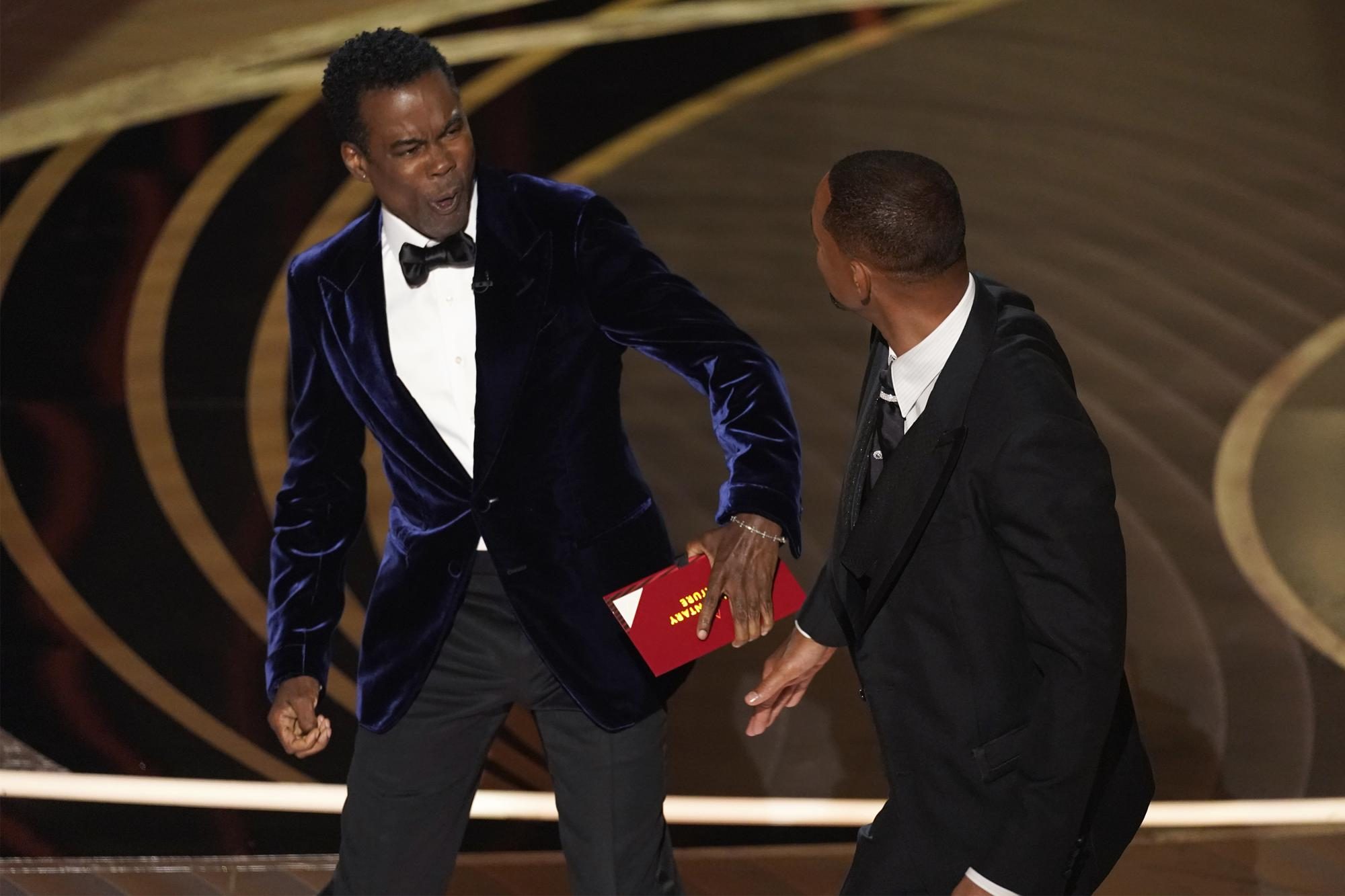 El presentador Chris Rock, a la izquierda, reacciona después de ser golpeado en el escenario por Will Smith mientras presentaba el premio a la mejor película documental en los Oscar el domingo 27 de marzo de 2022 en el Dolby Theatre de Los Ángeles.