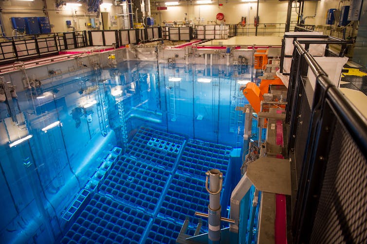 cientos de aberturas cuadradas yacen en el fondo de una gran piscina de agua en un edificio industrial