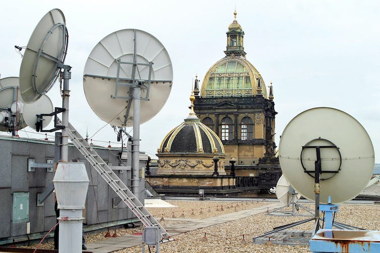 Las antenas parabólicas adornan un techo, con torres de iglesia al fondo