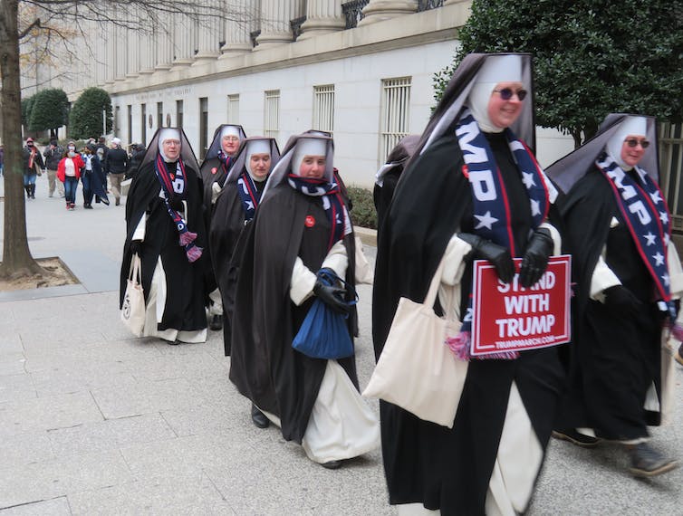 Un grupo de monjas marcha con hábitos completos, también con bufandas que dicen 'Trump' y con un cartel que dice 'Stand with Trump'.