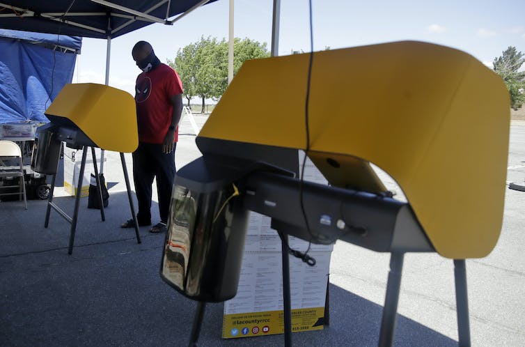 Un hombre se para en una cabina de votación al aire libre.