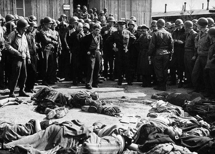 Una foto en blanco y negro muestra a soldados mirando cuerpos esparcidos en un patio.