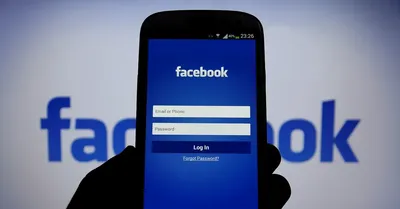 Un teléfono muestra la página de inicio de sesión de Facebook frente a un fondo que dice Facebook en azul. 